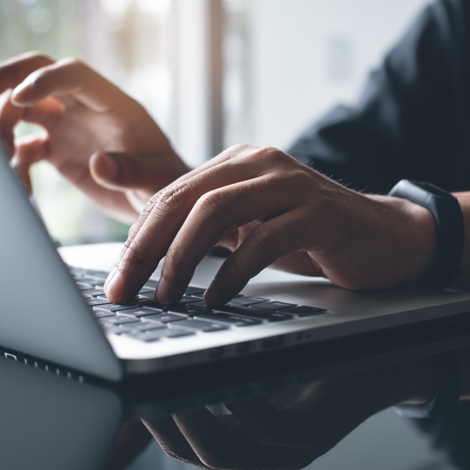 A person actively typing on a laptop, highlighting their hands on the keyboard and the bright display in front of them.