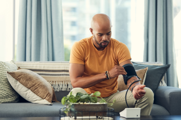 A person sits on the couch and checks their blood pressure.