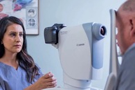 A person looks into an eye examination device while a medical professional assists.