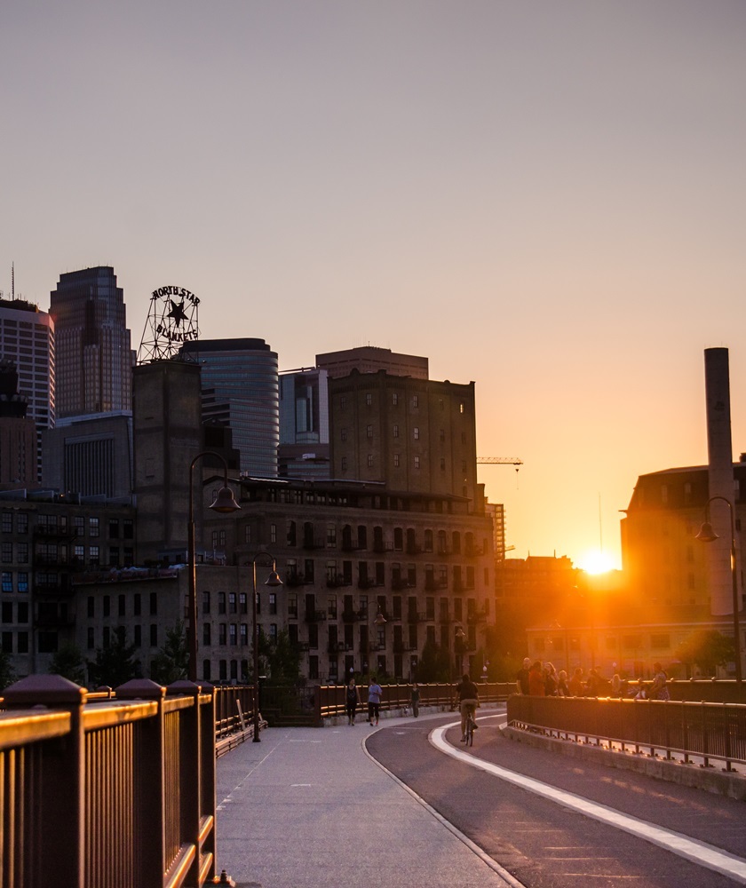 Sun rising behind a city scape with a pathway curving in front