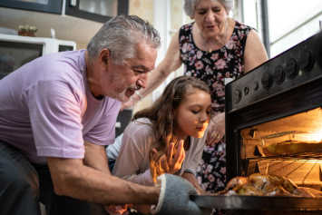Three people check on food cooking in an oven.