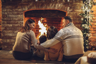 A couple and two small children sit facing a fireplace decorated with a holiday wreath.