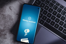 Smartphone resting on laptop with money transferred online on screen.