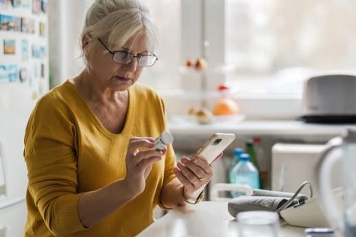 A person looks down at their phone and a prescription bottle.