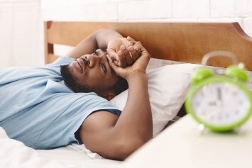 A person laying down in bed next to their alarm clock.