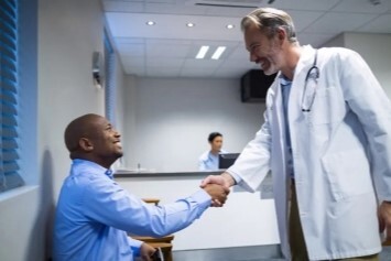A doctor shakes hands with a person sitting in a waiting room before their appointment.