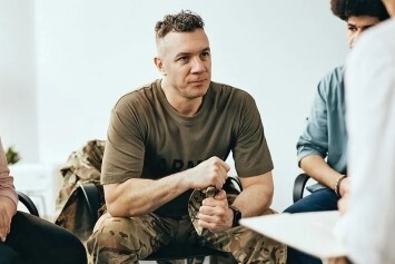 A person sits and speaks with a group.