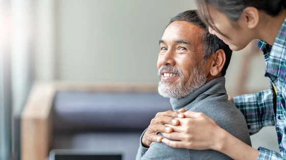 Smiling older man touching daughter's hand on shoulder.
