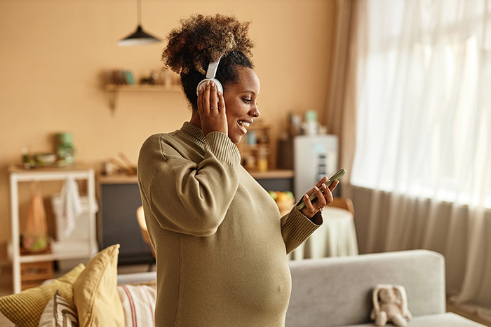 A pregnant woman checks her smartphone while wearing large headphones.