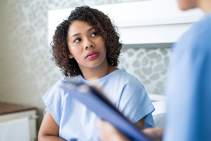A woman dressed in hospital gown listens to a health care professional.