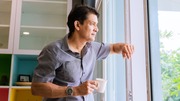 A man is holding a coffee cup while gazing out of a window.