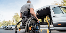A man in a wheelchair moves to the lift of a specialized vehicle.