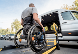A man in a wheelchair moves to the lift of a specialized vehicle.
