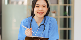 Female doctor sitting and holding a clipboard and looking at camera.