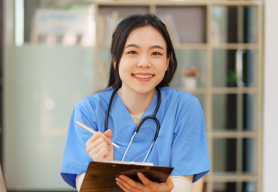 Female doctor sitting and holding a clipboard and looking at camera.