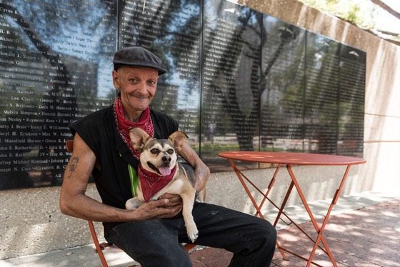 Older Veteran and dog sit in front of memorial wall