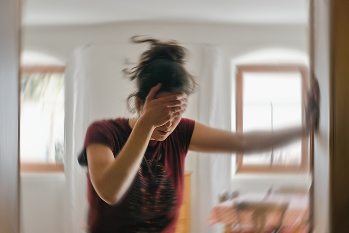 A woman covers her eyes in pain while holding onto the wall for support.