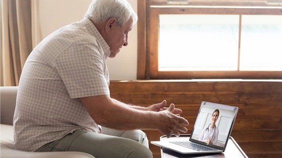 An older man is having a virtual call with a female doctor on his laptop.