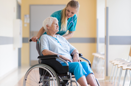 Senior woman in wheelchair with nurse in hospital.
