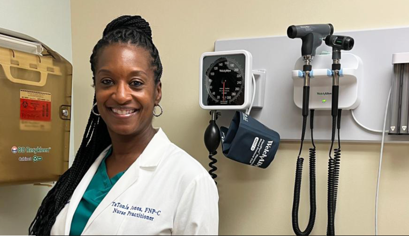 A smiling nurse practitioner stands in front of medical equipment