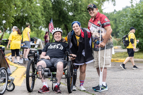 person in adaptive bicycle, person with prosthetic, person with crutches, all smiling 
