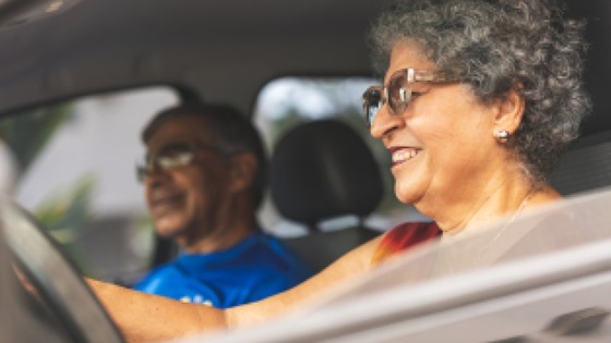 Elderly woman driving a car with an elderly man sitting in the passenger seat beside her.
