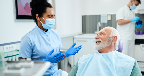 Senior man talking to female dentist during appointment at dental clinic.