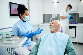 Senior man talking to female dentist during appointment at dental clinic.