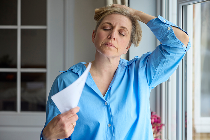 A woman wearing a blue shirt fans herself with a piece of paper.