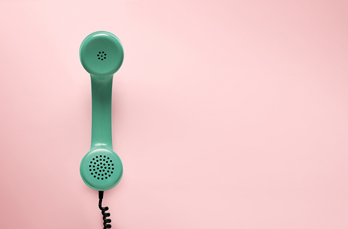 A green landline phone against a pink background.