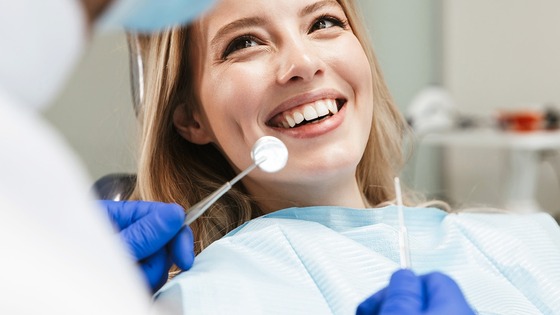 Dentist wearing blue gloves holding dental tools near a patient in a dental chair with a protective bib.