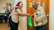 A woman hands a green reusable bag to an elderly man.