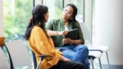 Two women seated in a waiting area, engaged in conversation.