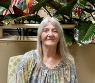 person smiling sitting in front of wall with plants and some flags 