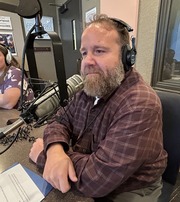 person with beard in a flannel in front of a studio microphone with a headset on