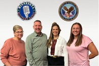 Three women and one man standing in front of a sign for MN Military Radio