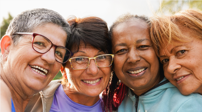 Four middle-aged women smile while embracing each other.