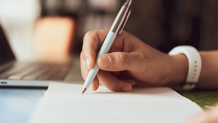 A woman writes a note on a pad of paper.