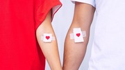 Two arms with adhesive bandages featuring red heart symbols after blood donation or vaccination.