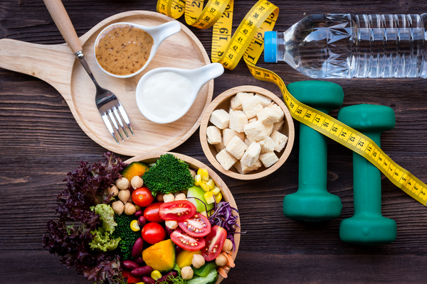 Variety of healthy foods, dumbbell weights, measuring tape and a bottle of water.