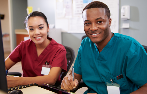 Male and female nurse smiling while at the receptionist desk.