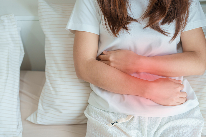 A woman cradles her abdomen in pain indicated by a glowing red light.