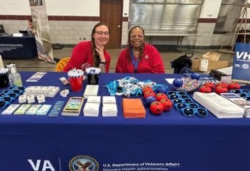 two people sitting a large table with a blue table cloth and lots of giveaways