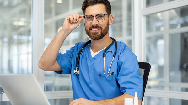 Male nurse smiling at desk with laptop.