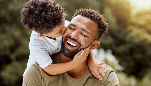 Dad and kid in a park enjoying nature hugging with care and a smile.