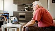 Elderly man sitting at a table, video chatting on a laptop.