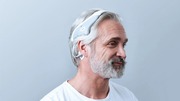 Side view of an elderly man wearing a white headband device.