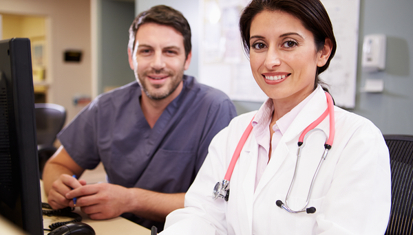 Female Doctor With Male Nurse Working At Nurses Station.