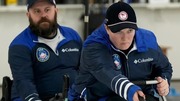 Two athletes in winter sports gear focused on their curling.