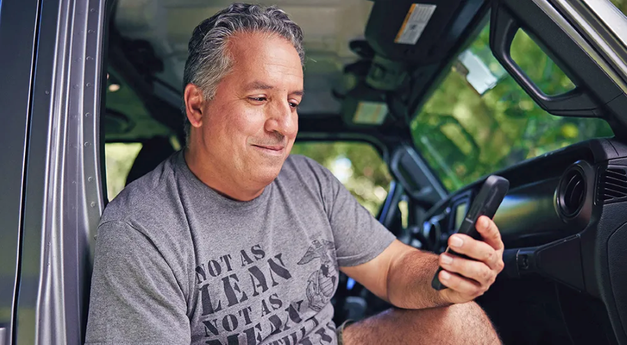A Veteran looks at their phone while sitting in their car